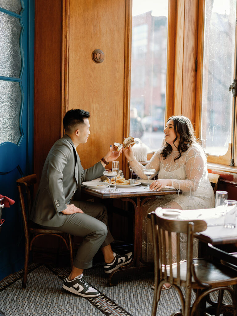 Couple cheers-ing with their cheeseburgers at Le Diplomate in Washington, DC. They are sitting at a table by the window.