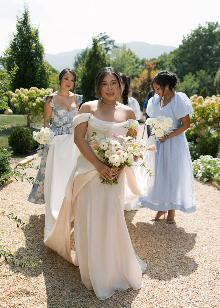 Bride and bridesmaids in soft blue and blush dresses walking garden path at The Seclusion