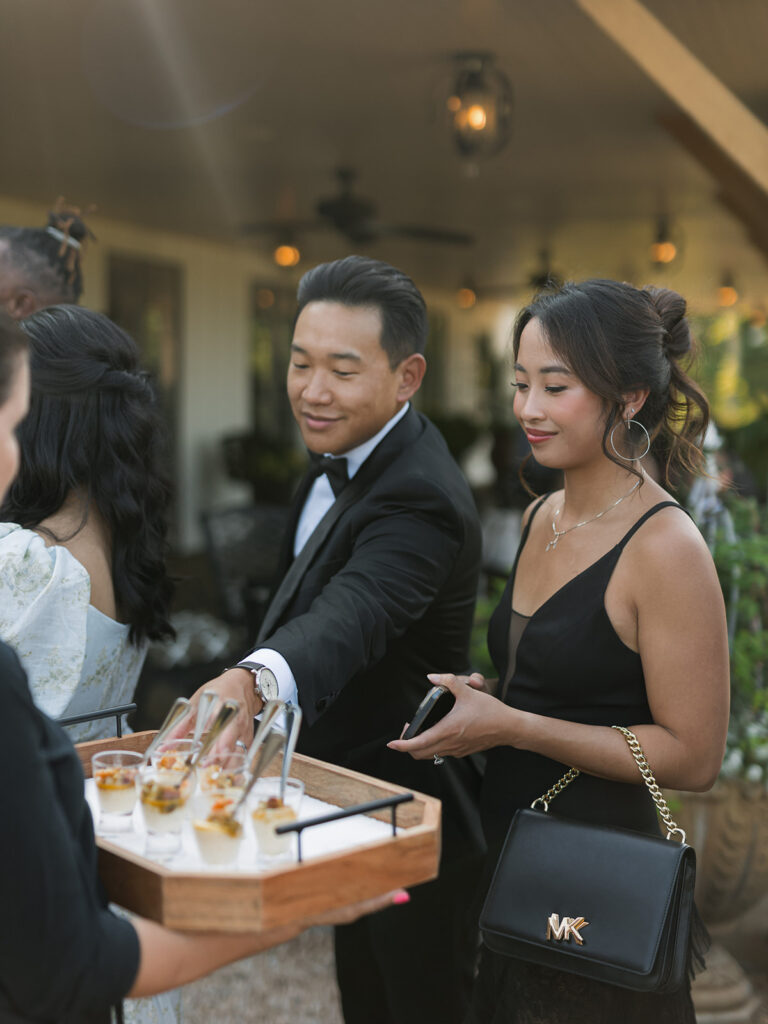 Wedding guests at cocktail hour selecting hors d’oeuvres from passed tray