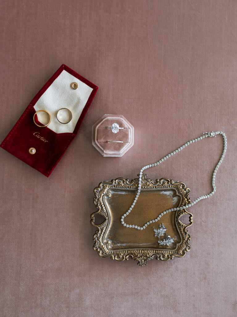 Cartier wedding bands, engagement ring, pearl necklace, and earrings styled on vintage tray and blush linen backdrop