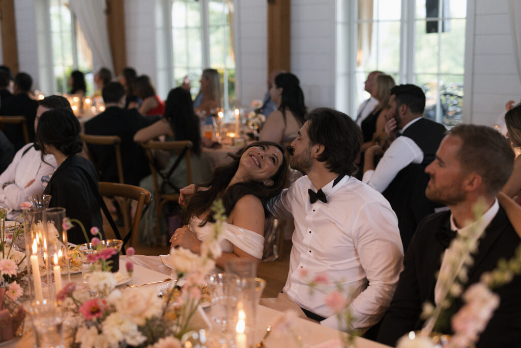 Bride and groom smiling at each other during wedding reception dinner surrounded by candles and florals