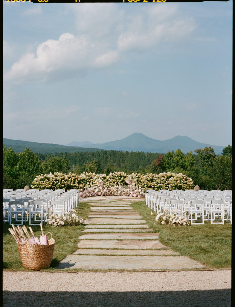 Ceremony Setup with Mountain View Rows of white chairs and a half-moon arrangement of blush flowers overlook a mountain view at an outdoor ceremony.