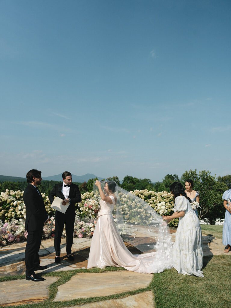 Ceremony Setup with Mountain View Rows of white chairs and a half-moon arrangement of blush flowers overlook a mountain view at an outdoor ceremony.