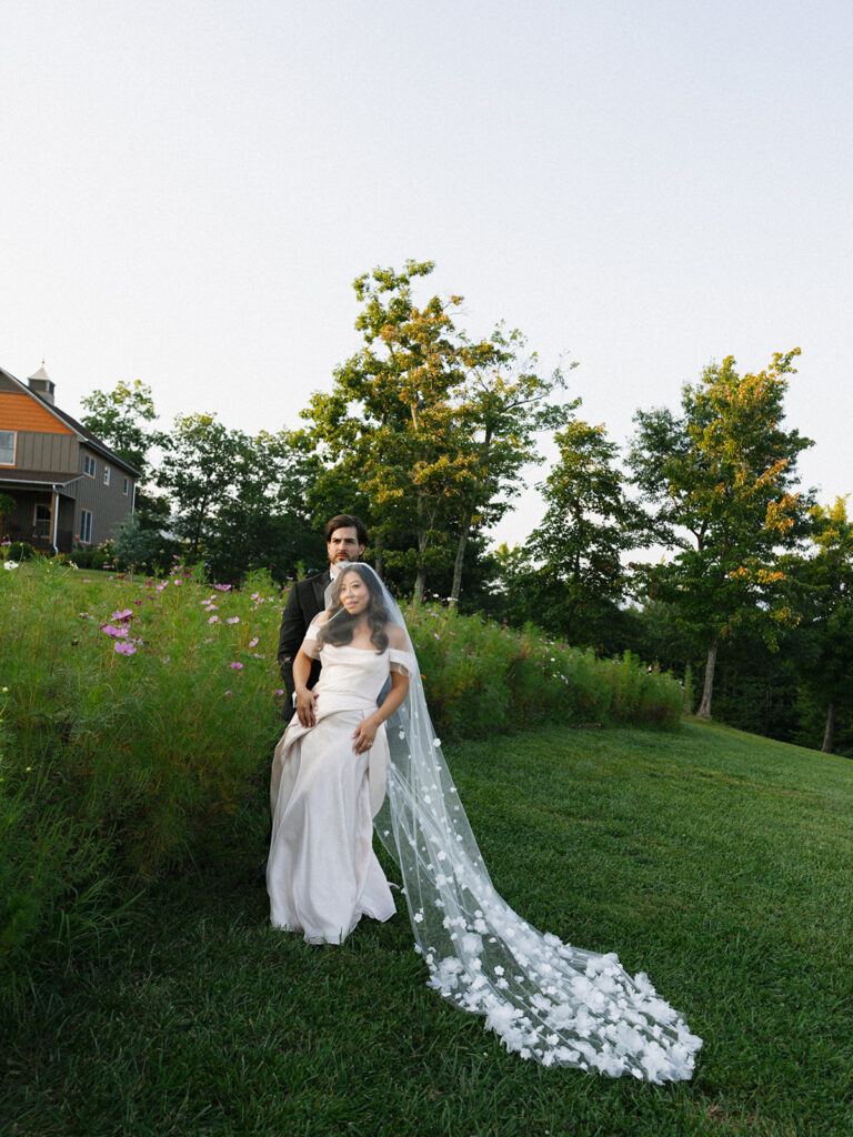 Golden Hour Portrait, Bride and Groom Walking Bride and groom walk hand-in-hand through sunlit wildflowers during golden hour.