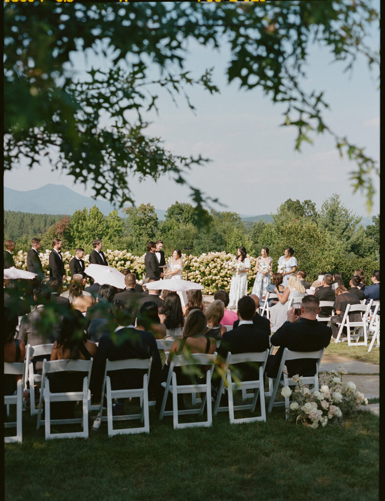 Ceremony Setup with Mountain View Rows of white chairs and a half-moon arrangement of blush flowers overlook a mountain view at an outdoor ceremony.