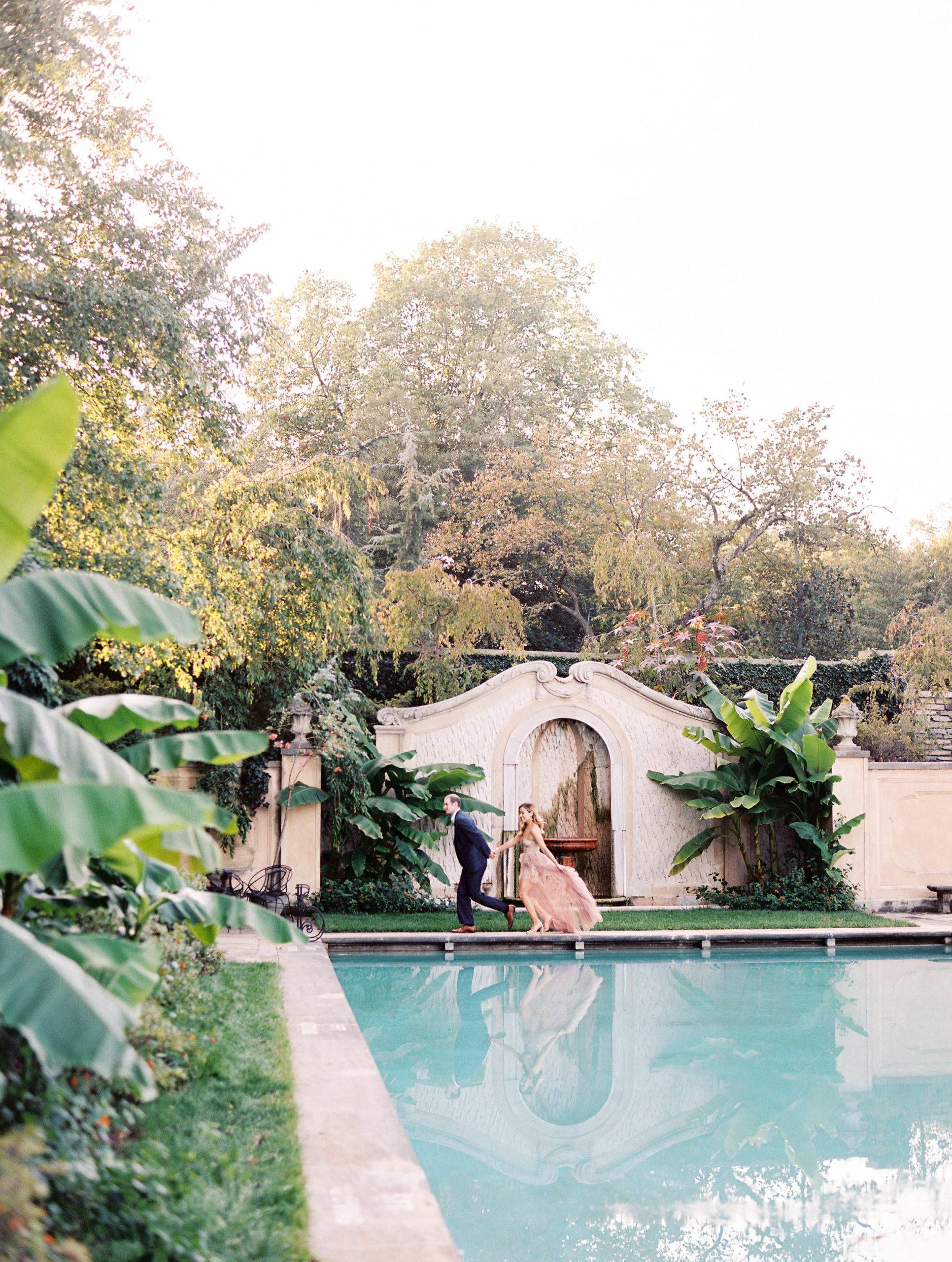 Couple running next to a pool in a tulle gown for engagement photos.