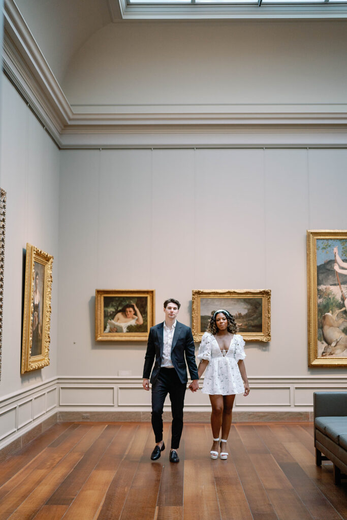 Engagement photos of a couple inside the National Gallery of Art Museum in Washington, DC. They sit together on a bench. Man is posing in front of a painting.