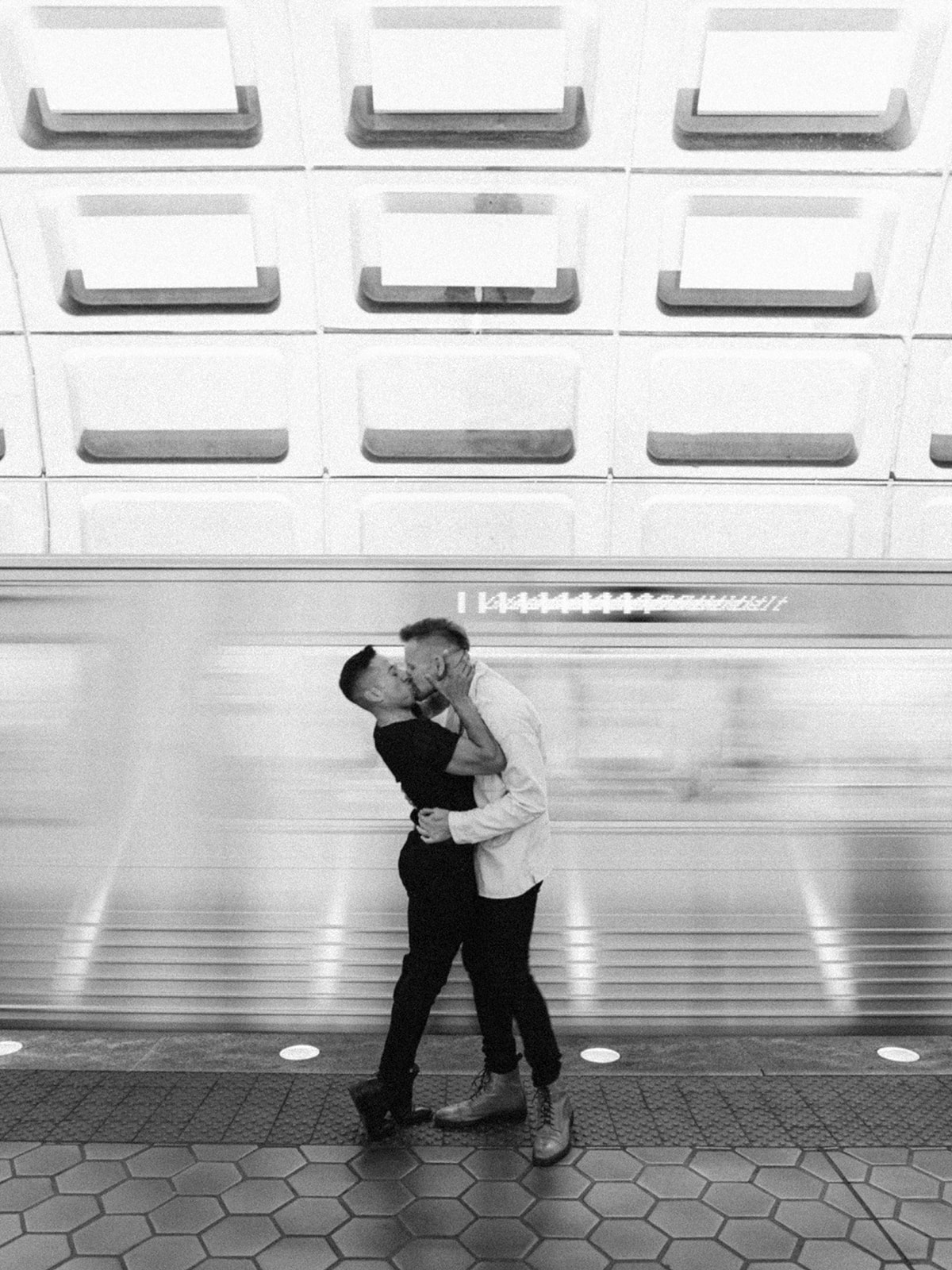 Gay couple kissing in front of a moving train at the DC metro station.