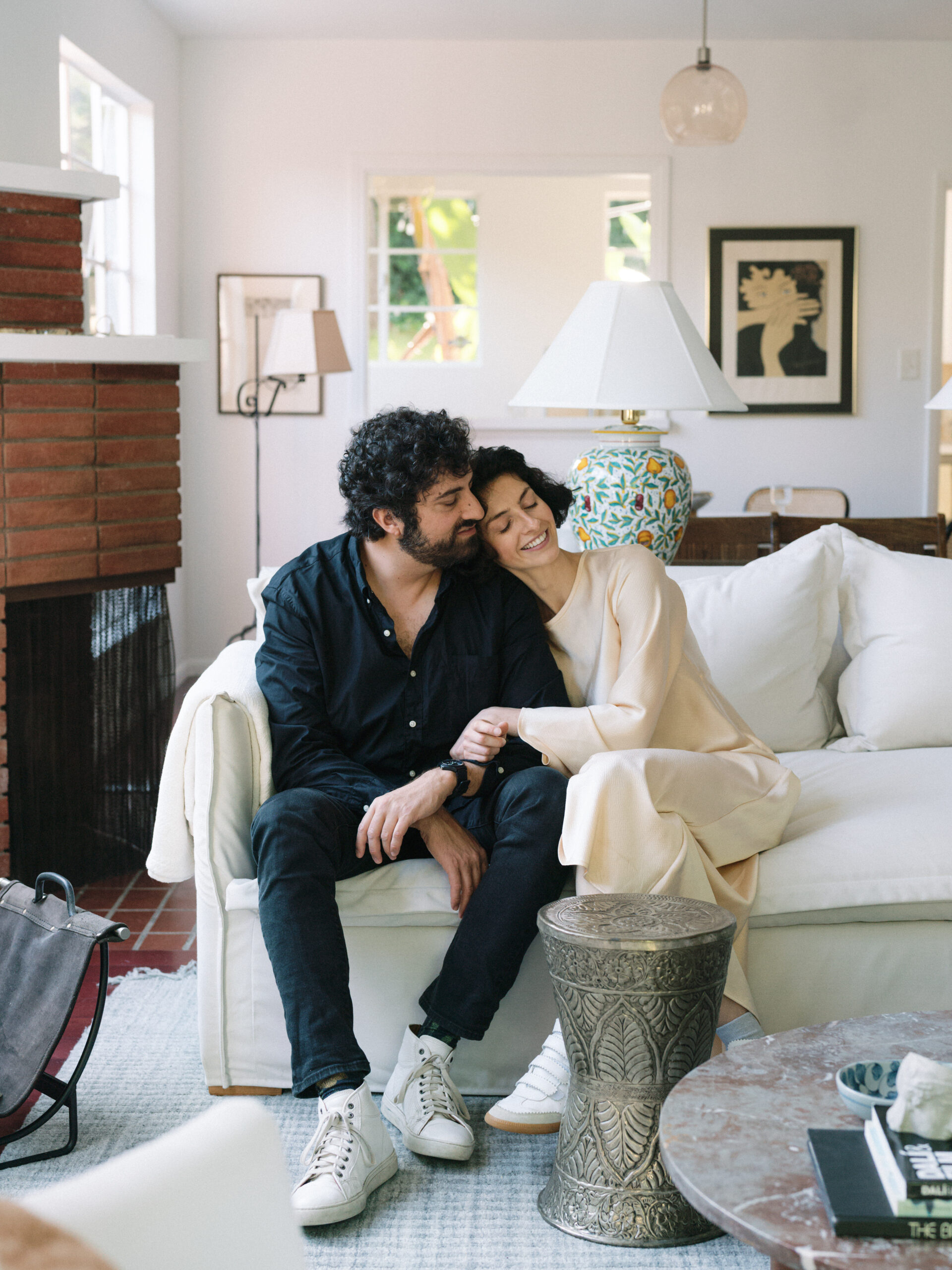 Couple cuddling on a white couch during an engagement photo session.